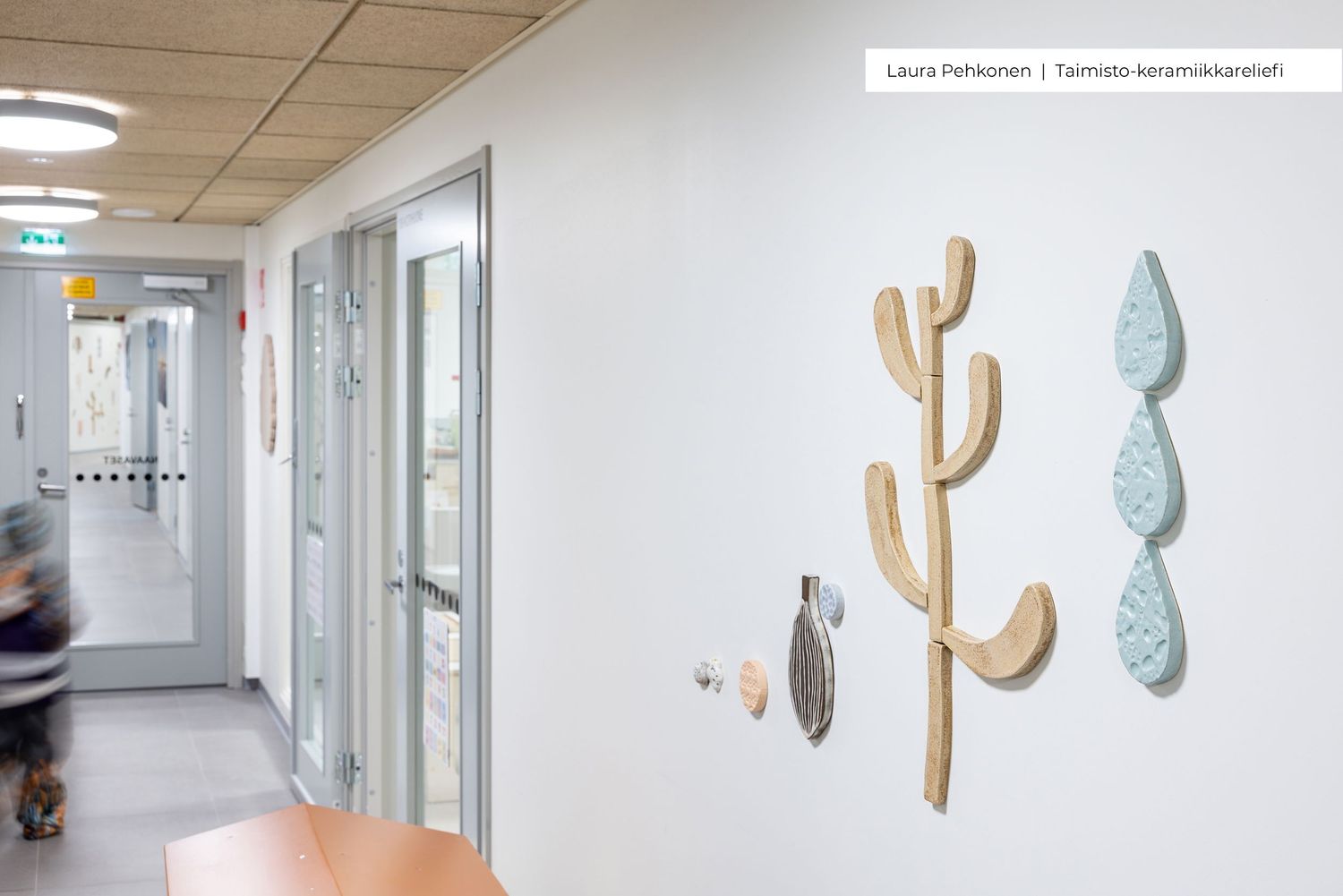 Ceramic wall art installations in a hospital corridor featuring nature-inspired sculptures by Laura Pohjoinen and Taimiola.