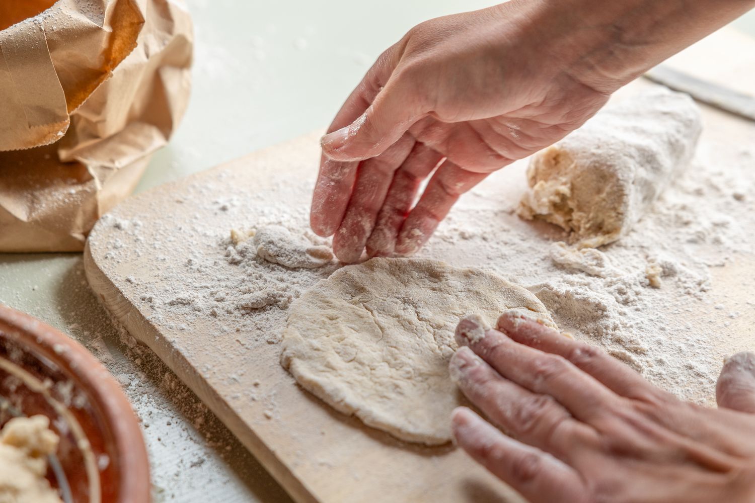 Hands kneading fresh dough on a floured wooden board during homemade bread or pasta preparation.