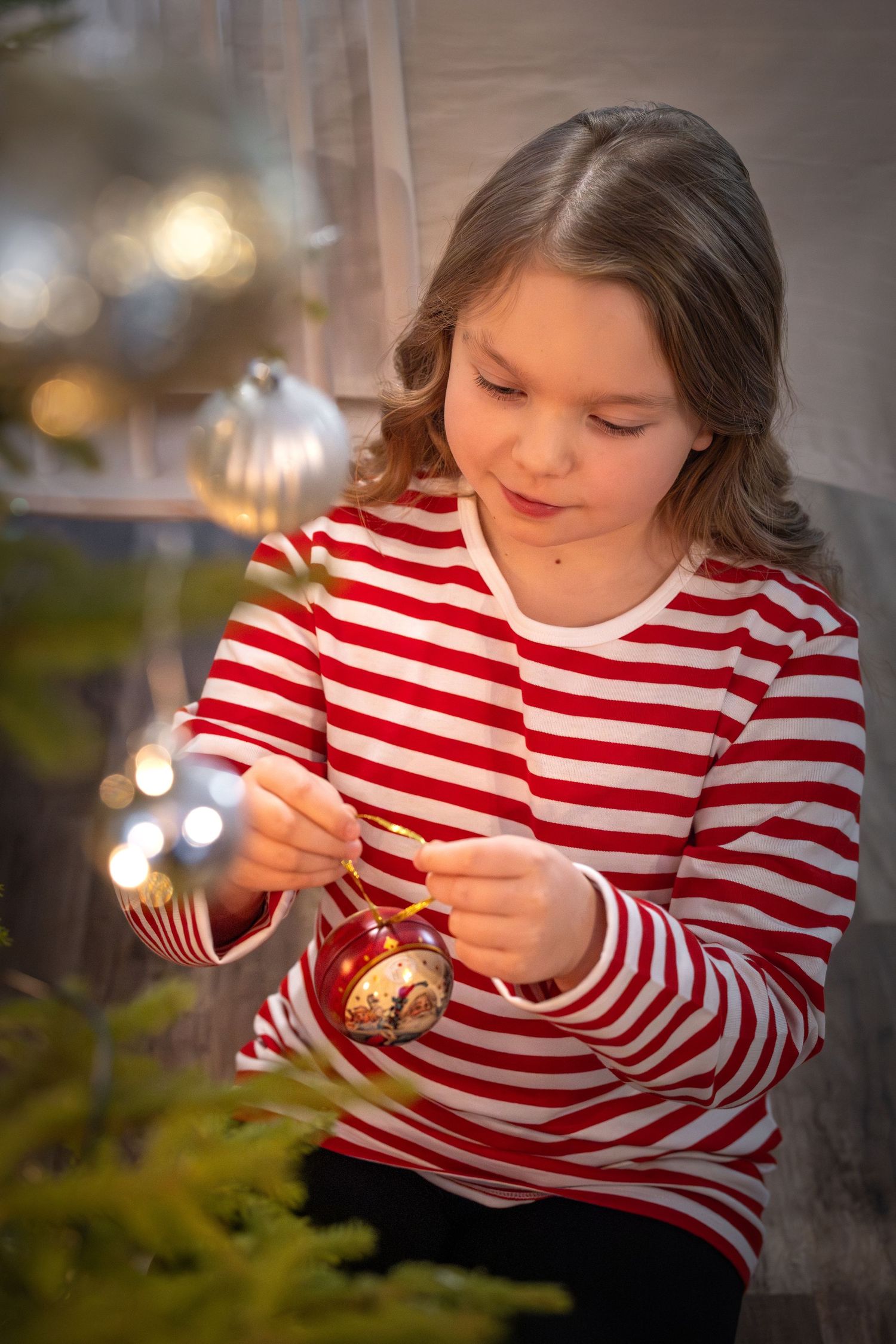 A person in a red and white striped shirt examines a Christmas ornament in a series of sequential photos.
