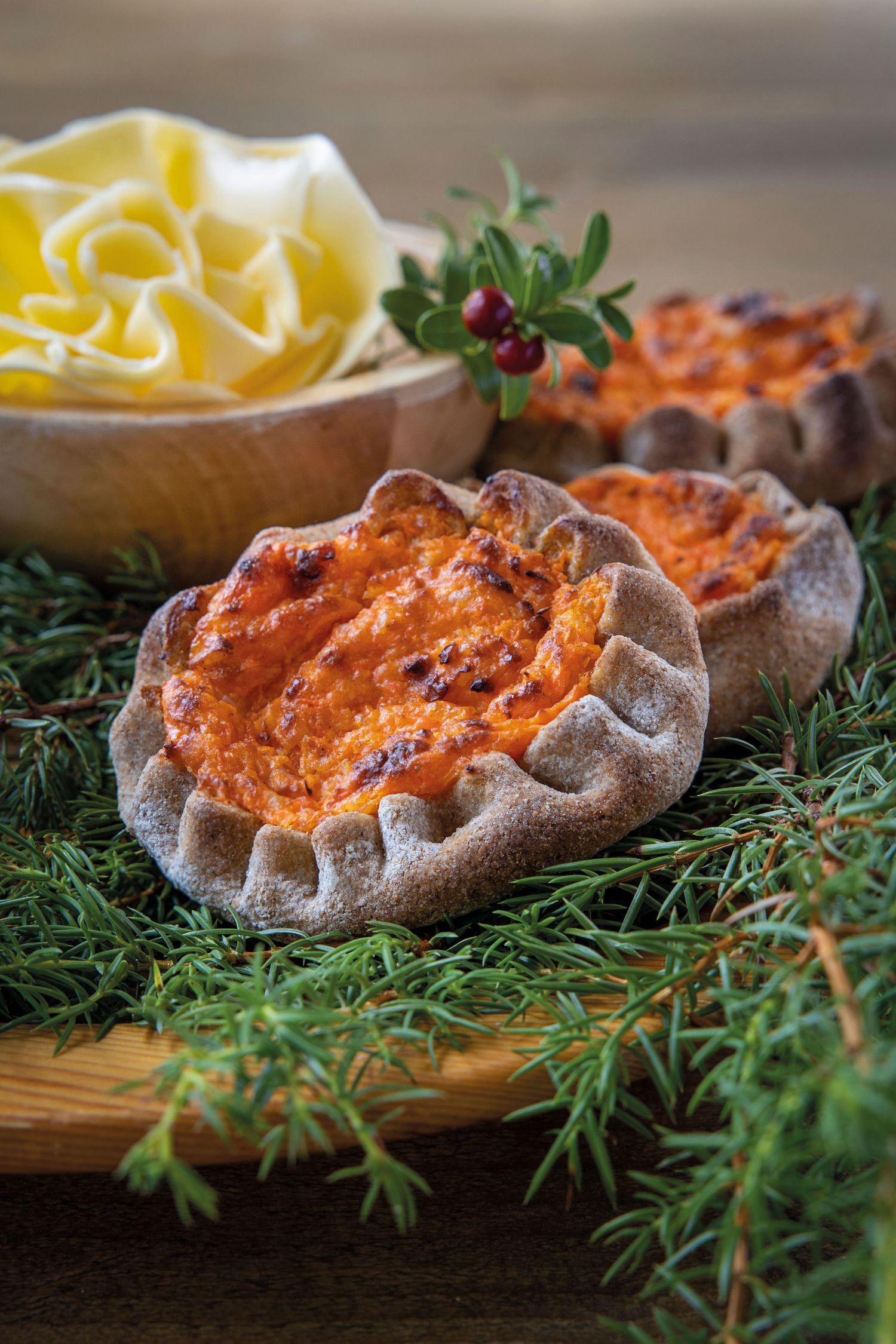 Traditional Finnish Karelian pies with carrot filling on pine branches, served with egg butter on wooden board.