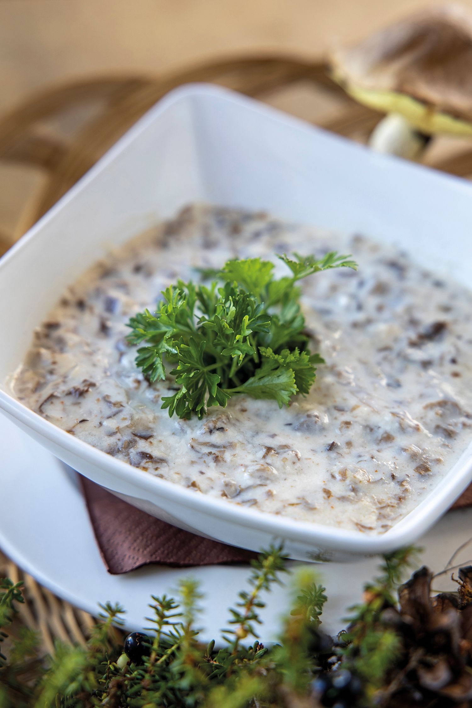 Creamy mushroom dip garnished with fresh parsley in a white square bowl, served on a woven mat.