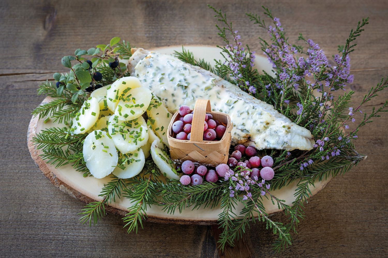 Rustic wooden board with sliced hard-boiled eggs, herb cheese, fresh grapes, and aromatic herbs on a wooden table.