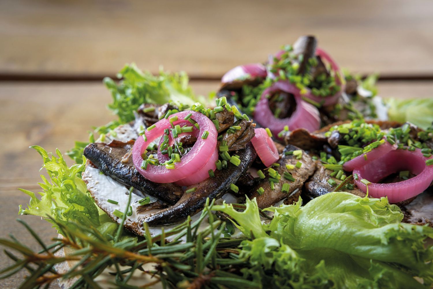 Grilled mushrooms on fresh greens with pickled red onions and herbs on a rustic wooden table.