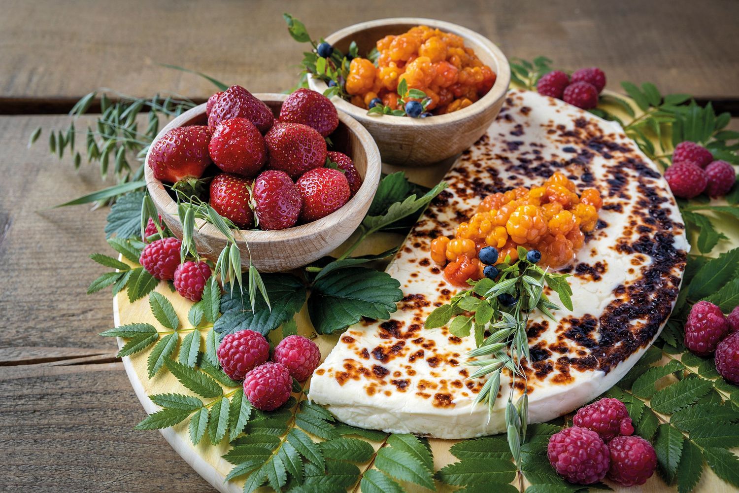 Grilled halloumi cheese on marble board with fresh raspberries, sea buckthorn berries in wooden bowls, garnished with green leaves.