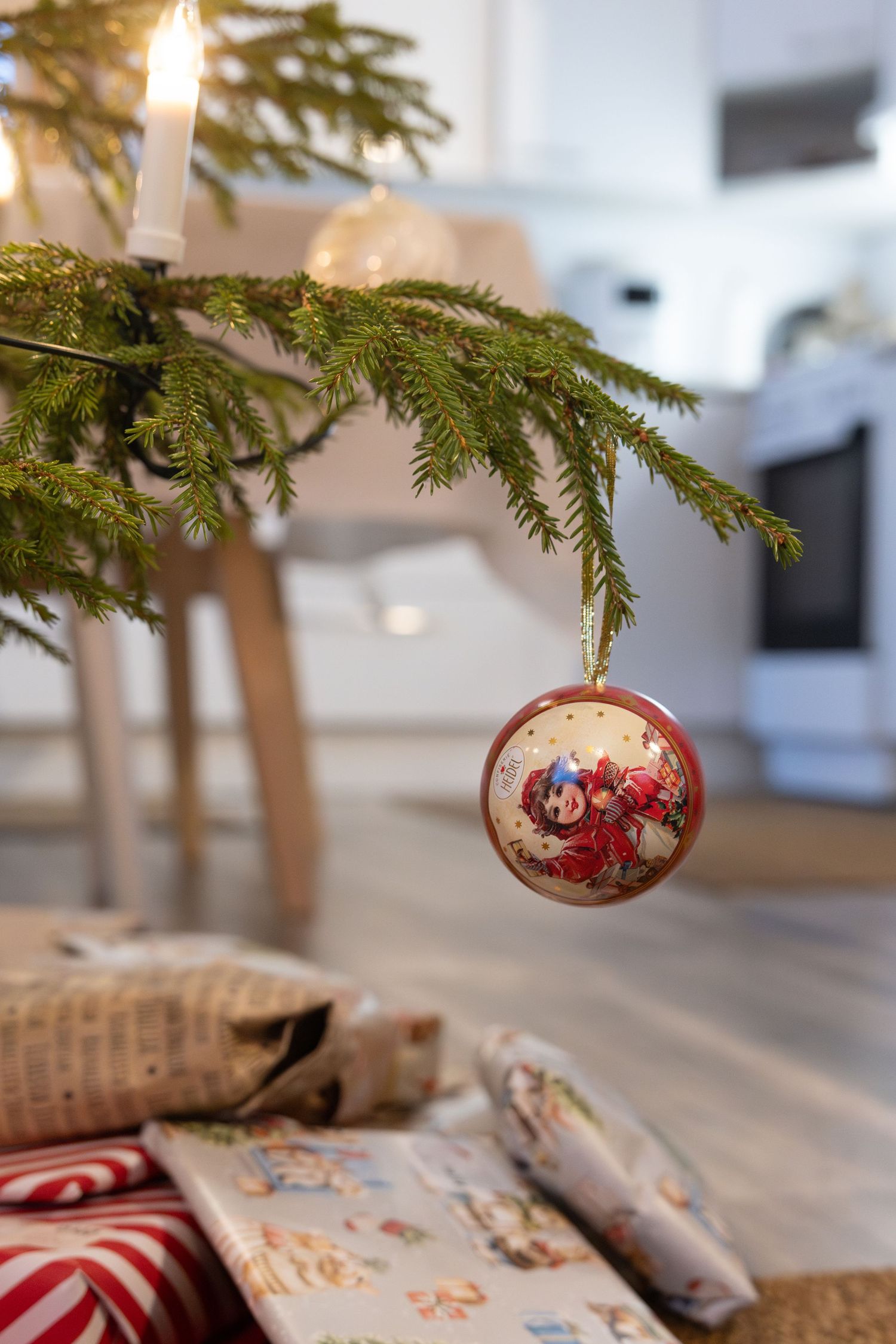 Christmas ornaments hang from evergreen branches over wrapped presents and candy canes in a cozy holiday setting.