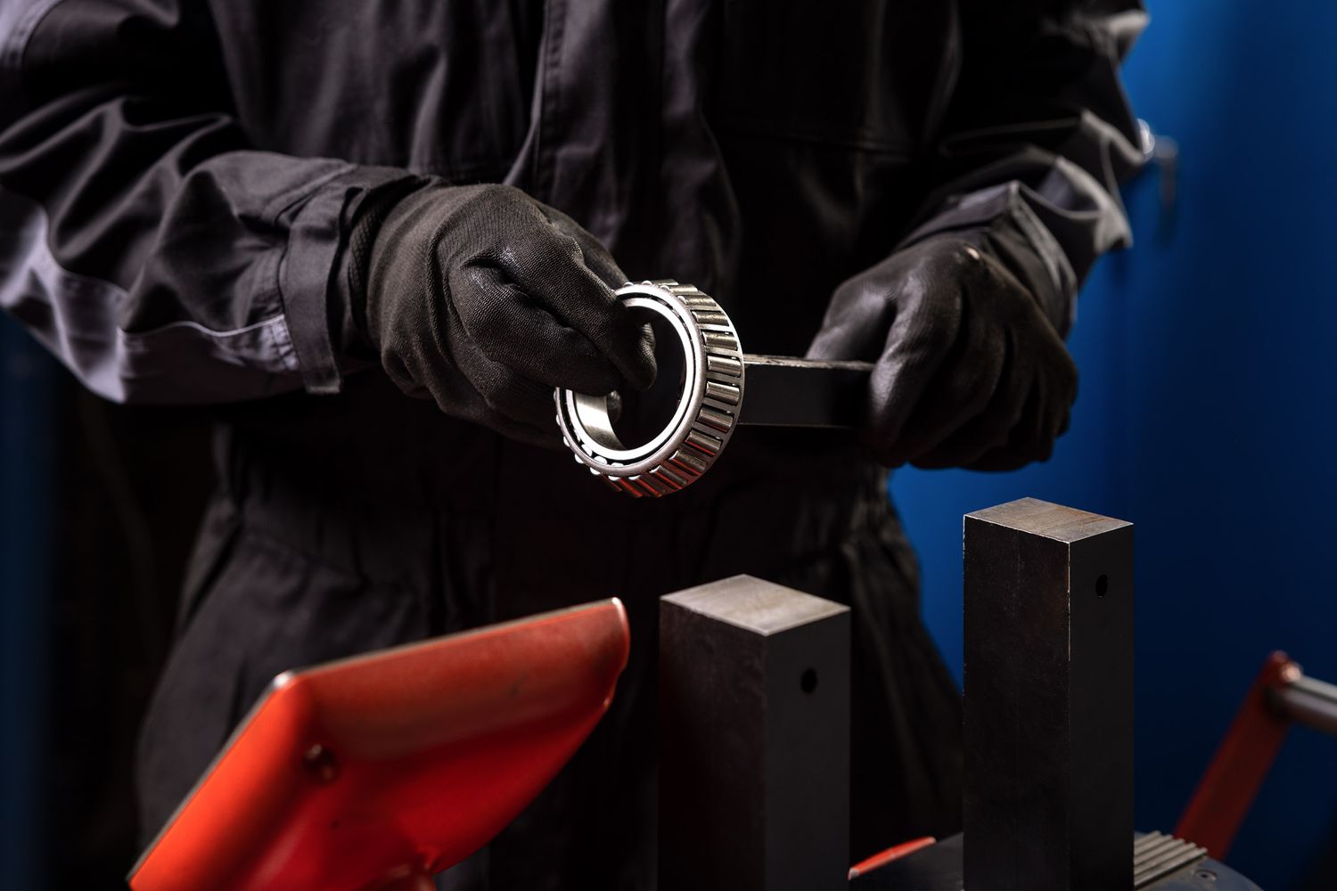 Mechanic in black gloves inspecting a roller bearing component in an automotive repair workshop.