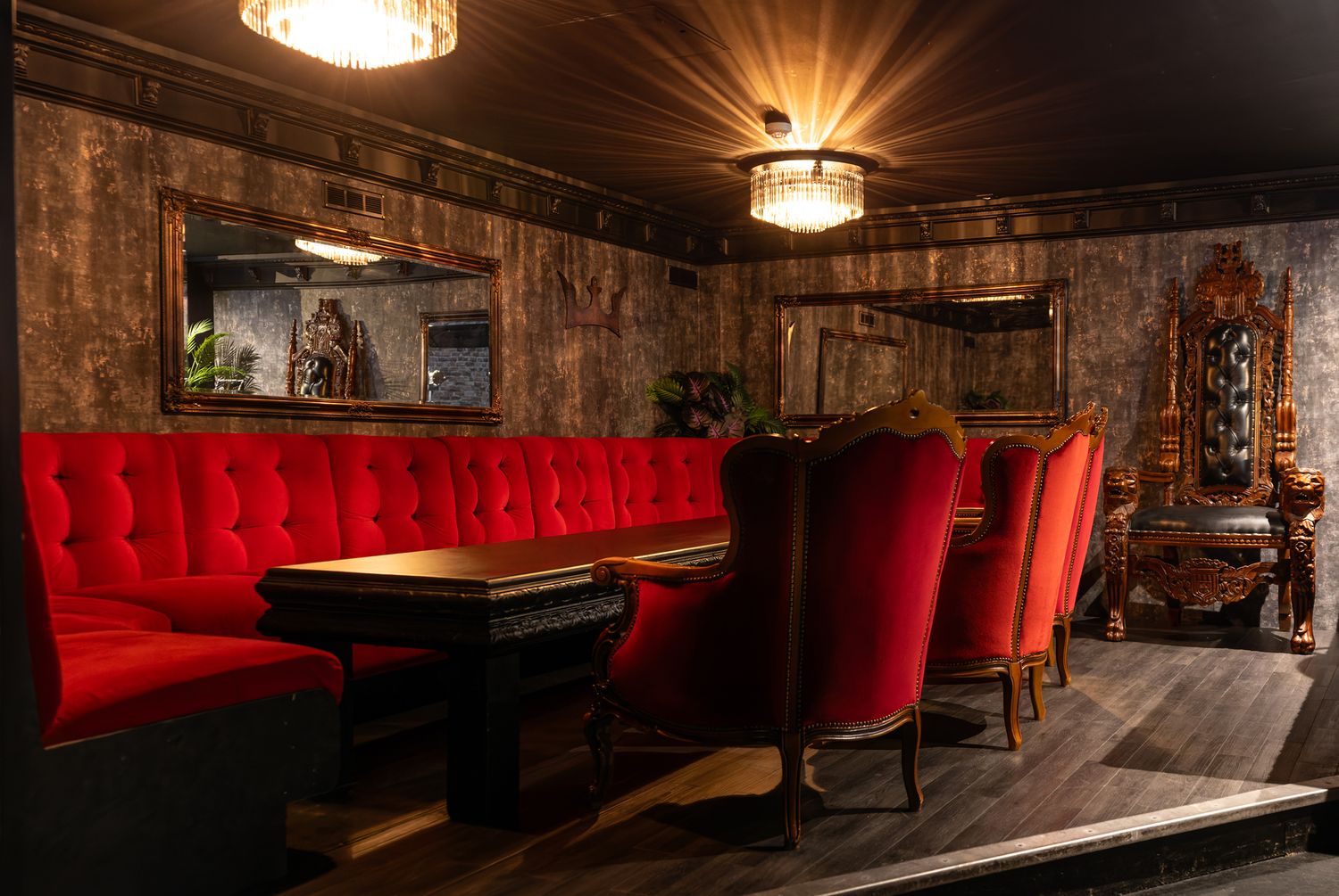 Elegant bar lounge with red tufted velvet banquette seating, vintage chairs, and dark wood paneling under warm lighting.
