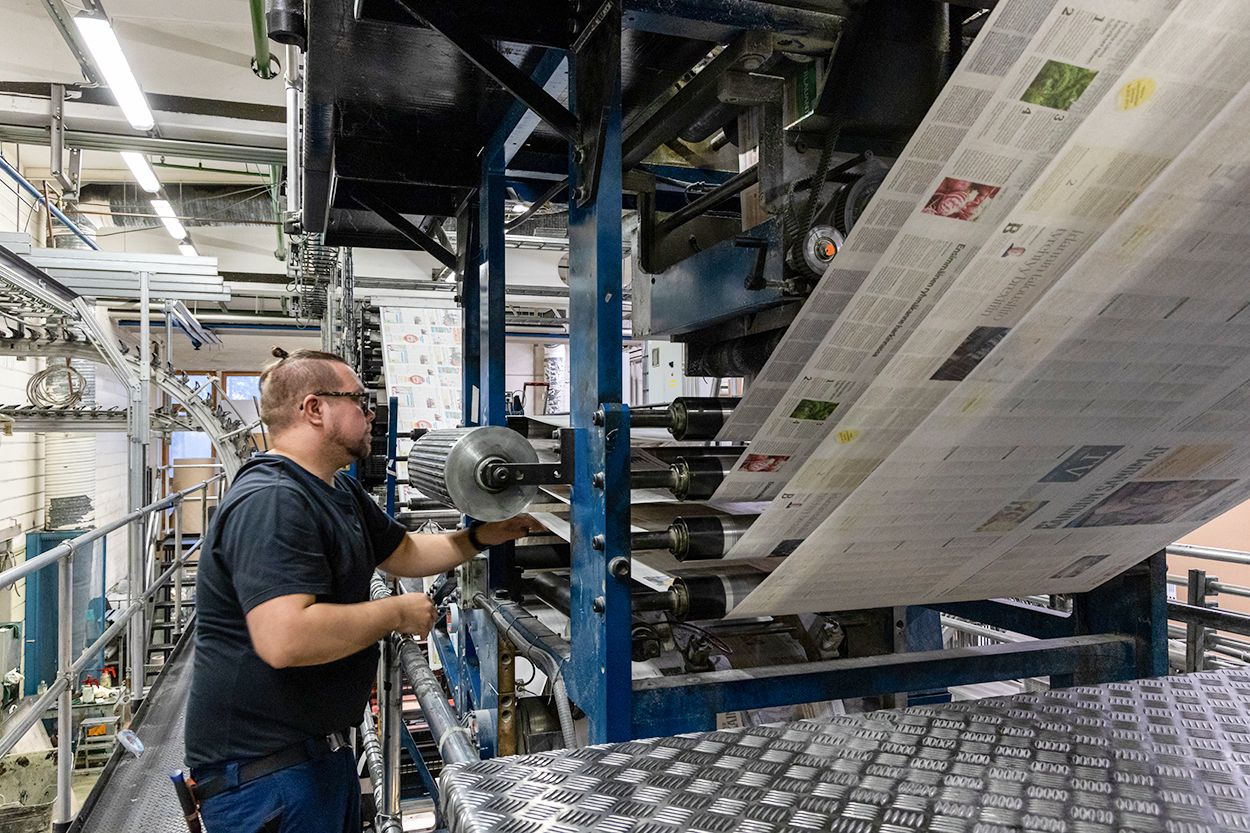 Lehtipainon työntekijä tarkastaa painokonetta. Painokoneessa painettua paperia.