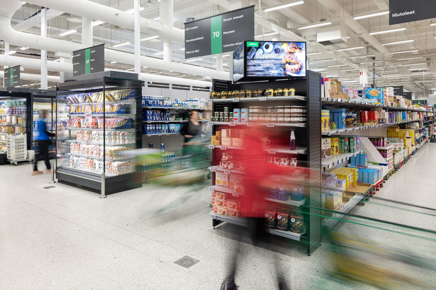 Supermarketin käytäviä, ohikiirehtiviä ihmisiä epäterävänä.
