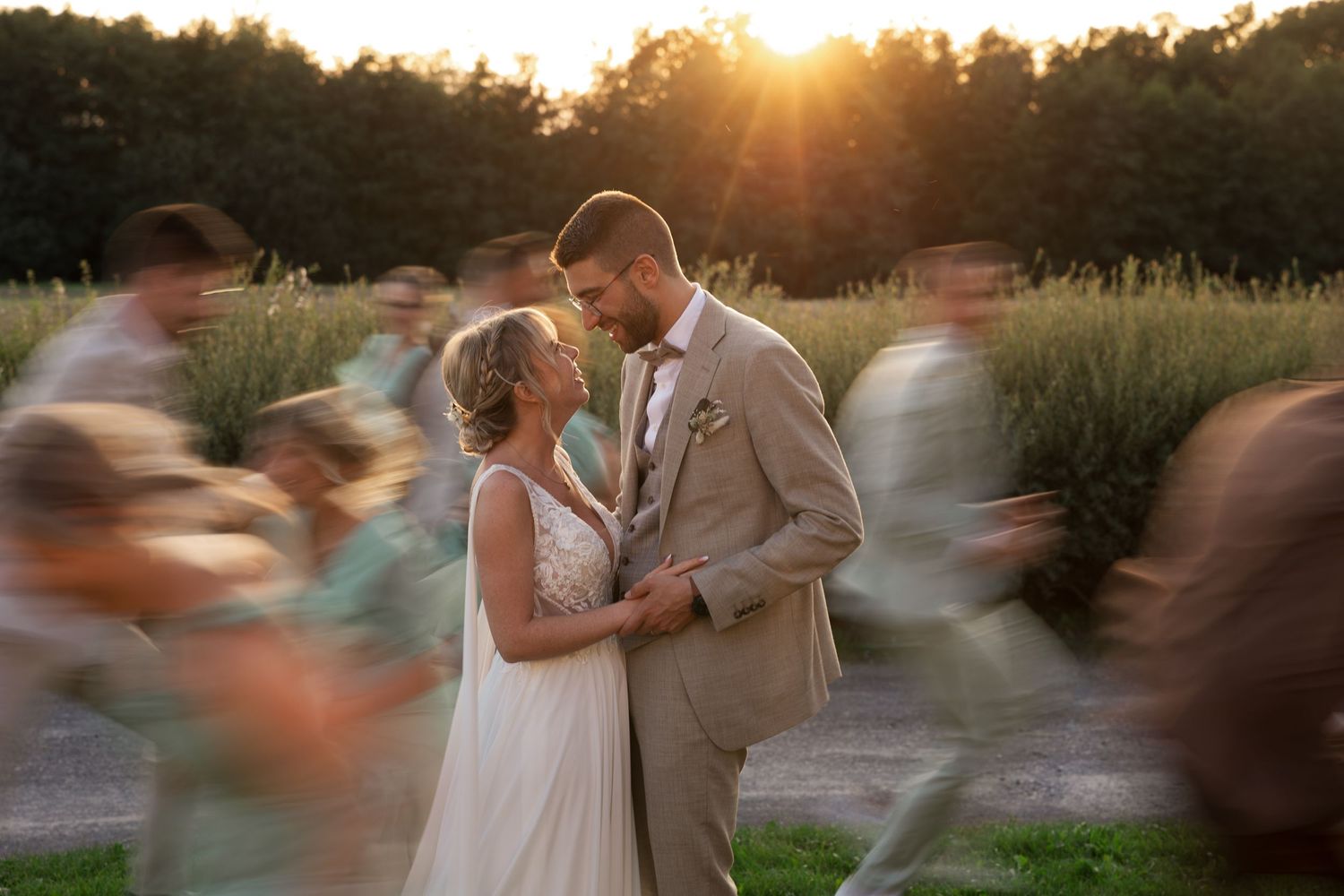 A joyful wedding couple shares an intimate moment as guests blur past in the golden sunset light.
