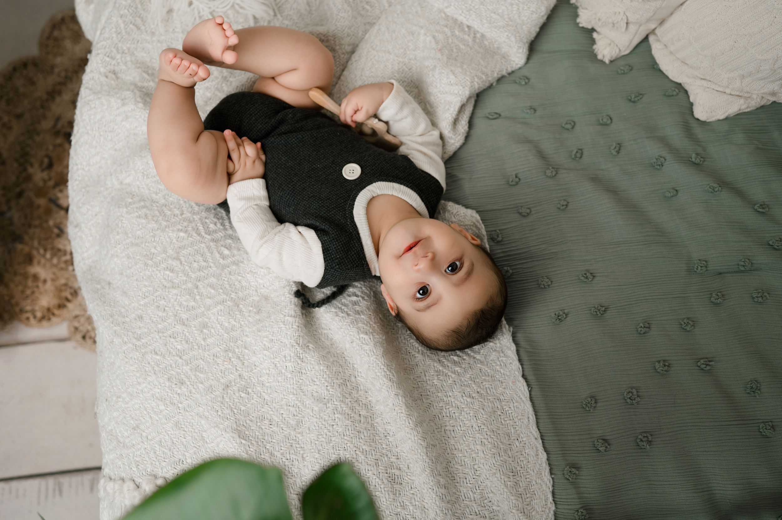 A small child wearing a black and white outfit lies on a white blanket next to a green cushion.