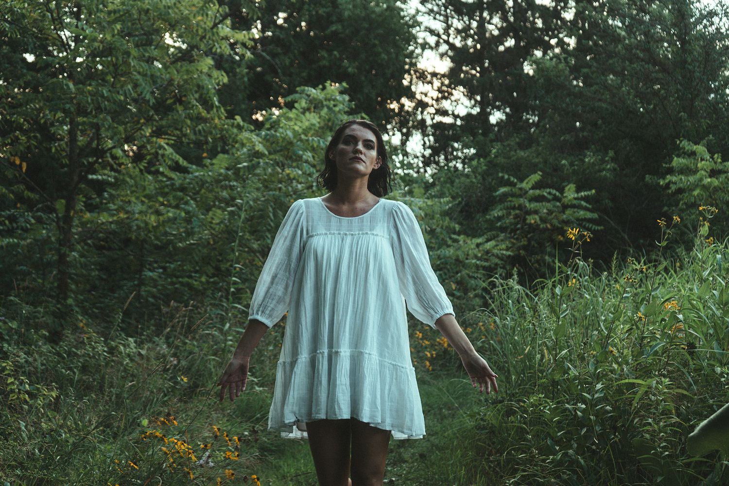 A person in a flowing white blouse poses gracefully walking through a meadow with wildflowers.