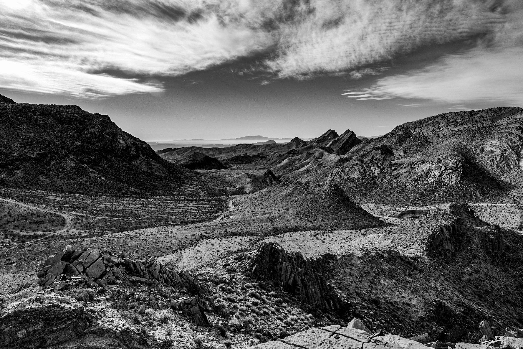 Black and white aerial view of rugged desert canyon landscape under dramatic cloudy sky.