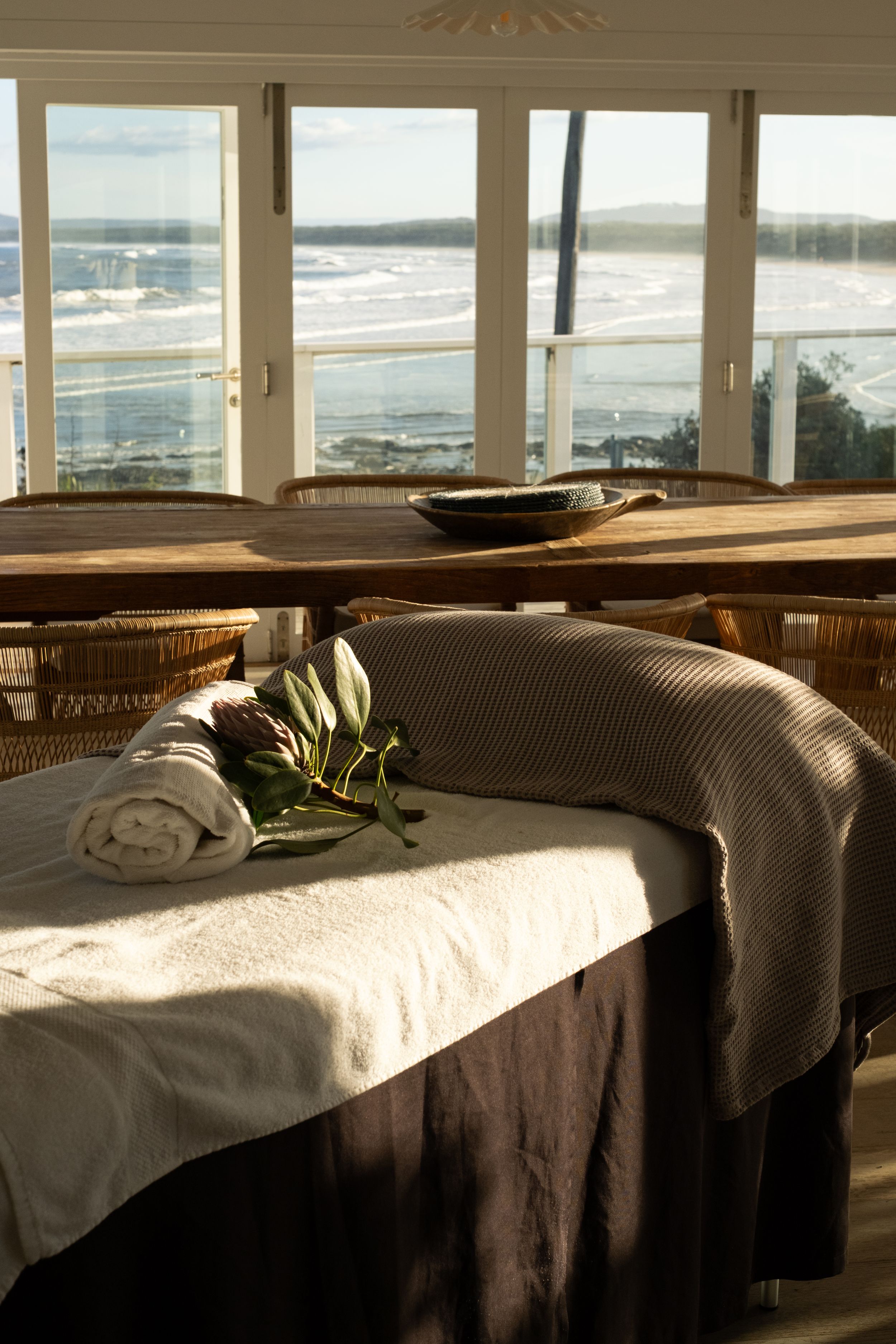 Sunlit spa treatment room with massage tables and panoramic ocean views through large windows.