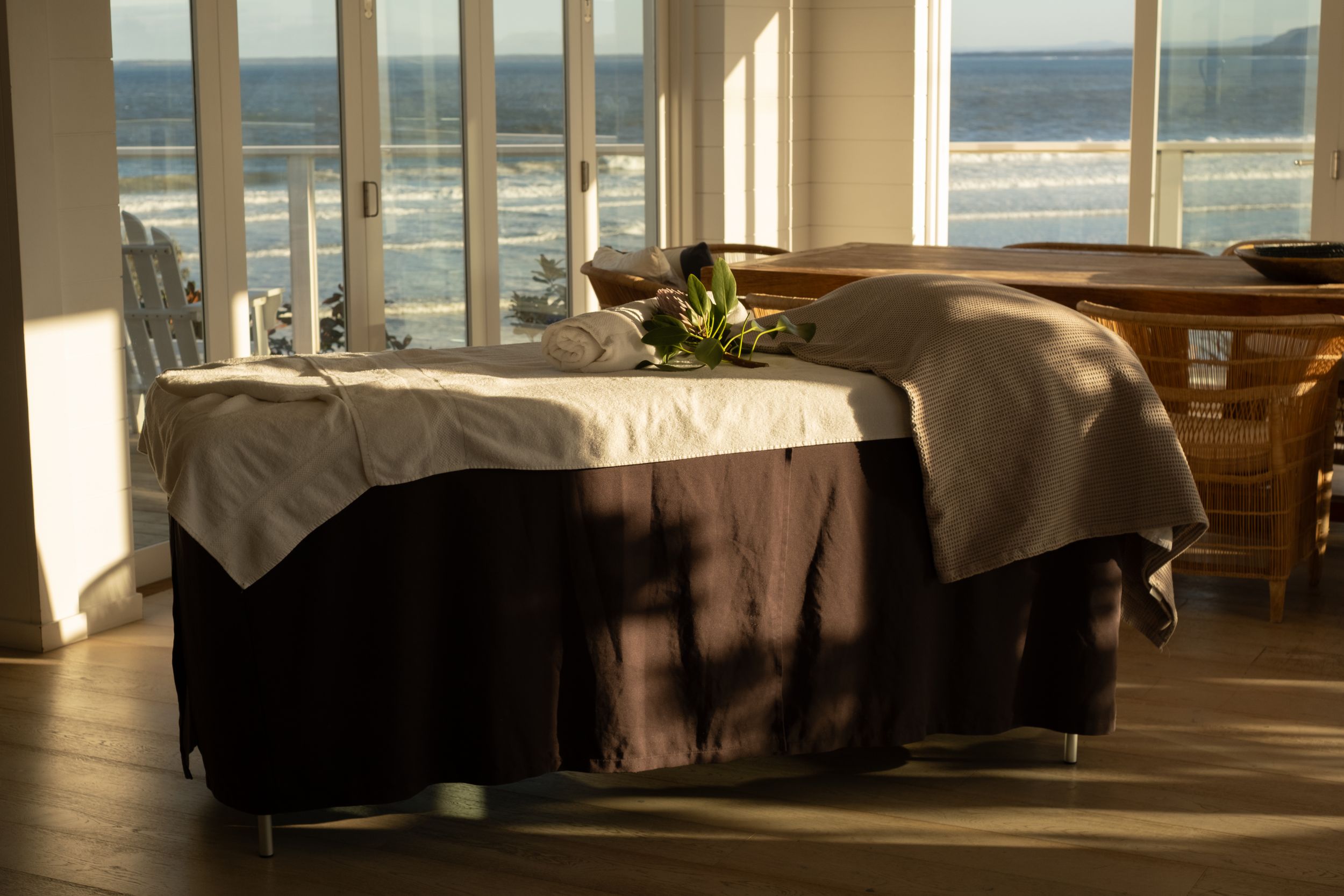 Massage tables lined up in a spa room with large windows overlooking an ocean view.