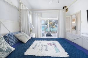 Bright white bedroom with blue bedding and multiple windows offering natural light and coastal views.
