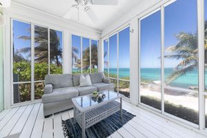 Panoramic beachfront room with floor-to-ceiling windows showcasing turquoise ocean views and white sand beach.