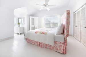 Minimalist white bedroom with soft pink accents and abundant natural lighting.