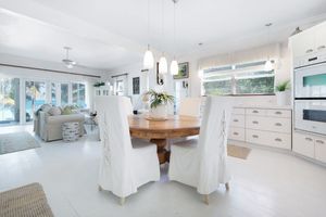 Open concept coastal style kitchen and dining area with white cabinetry, slipcovered chairs and round wooden table.