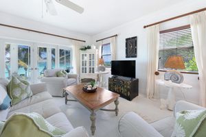 Bright coastal living room with white furniture, light green accents, tiled floors and elegant wooden coffee table.