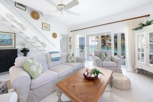 Bright coastal living room with white slip-covered furniture, wood coffee table, and large glass doors overlooking the ocean.
