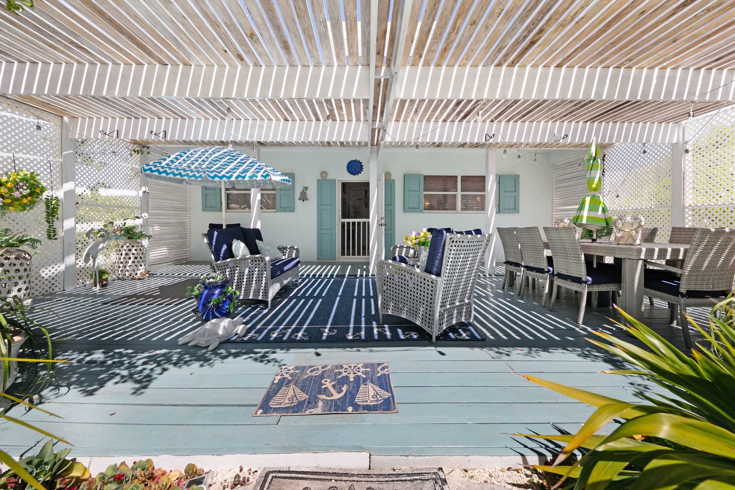Modern outdoor patio with slatted pergola, nautical decor, and comfortable seating arrangements overlooking the garden.