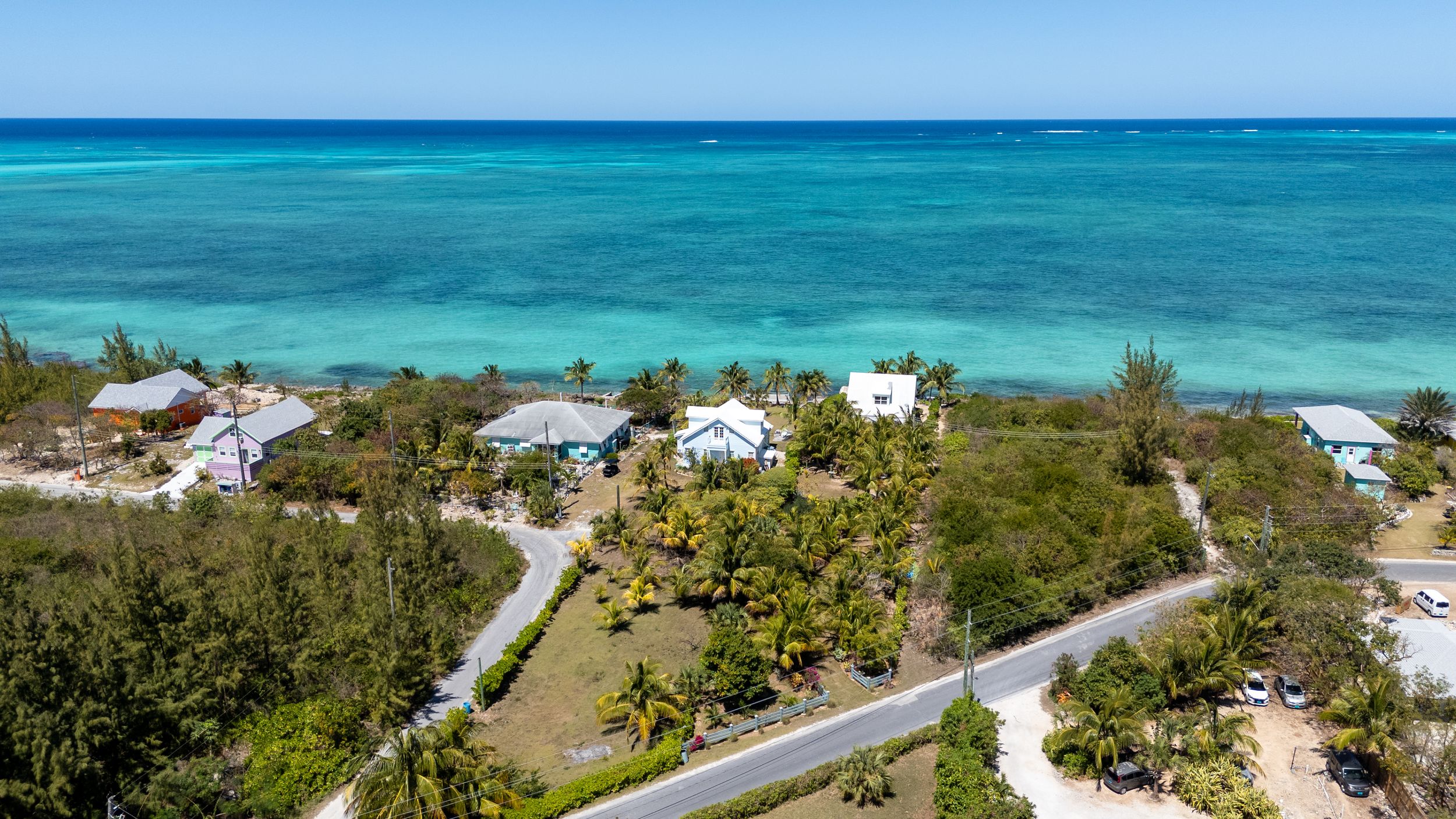 Aerial view of turquoise Caribbean waters with beachfront homes and winding roads along a tropical coastline.