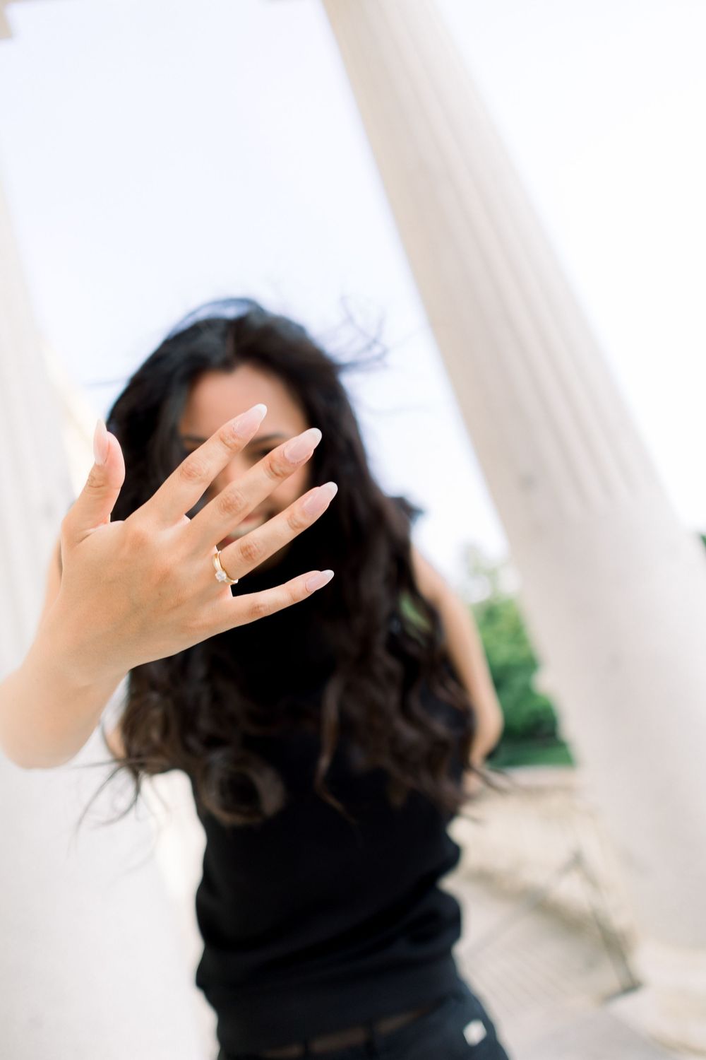 A woman in black with long dark hair holds up her hand showing an engagement ring.