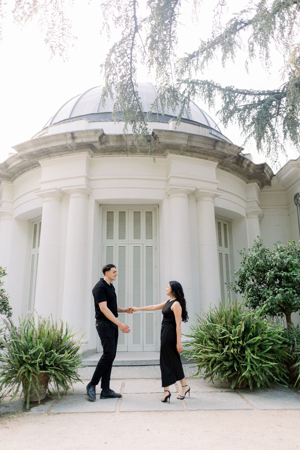 Couple in black attire holding hands in front of a classical domed building with columns.