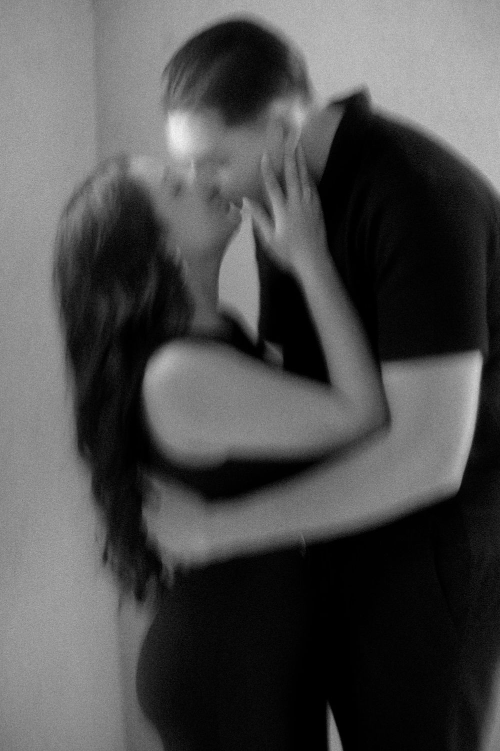 A romantic black and white photo captures an intimate embrace and kiss between two figures in soft focus.