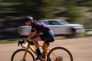 A cyclist in purple jersey rides a gold road bike with motion blur effect in the background.