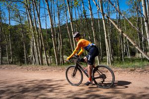 Mountain biker pedaling through an aspen grove on a dirt trail on a sunny day.