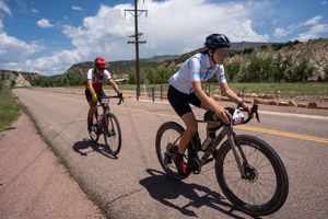 Cyclists riding road bikes along a paved mountain road under blue skies and white clouds.