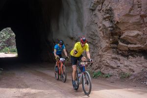 Cyclists ride through natural rock tunnel on mountain bikes during adventure trail ride.
