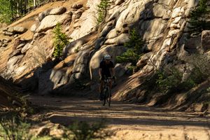 A mountain biker pedals past dramatic granite rock formations on a wooded trail.