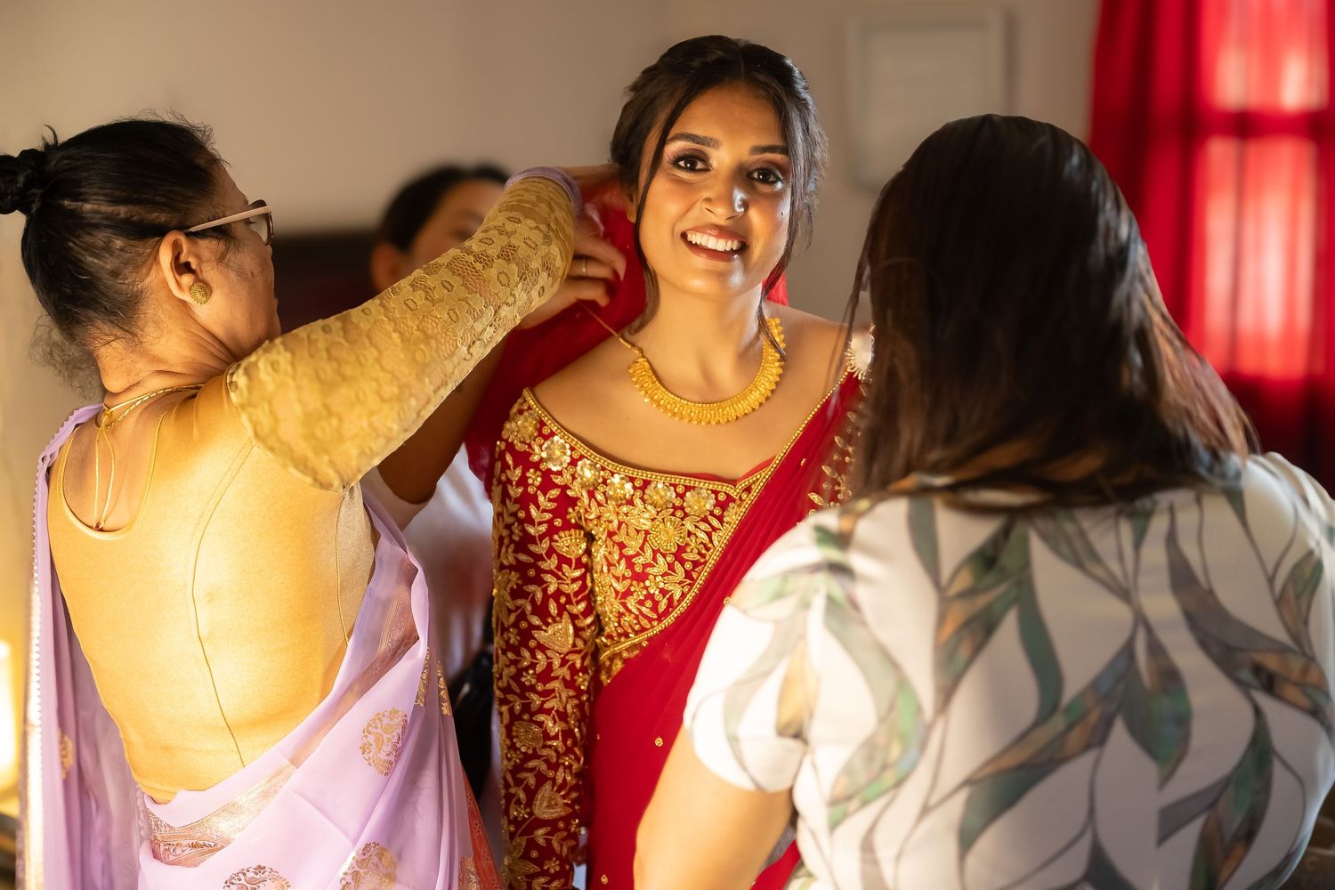 Nepali bride Mamta in a stunning red and gold traditional embroidered weddingdress is being helped with preparations on her wedding day.