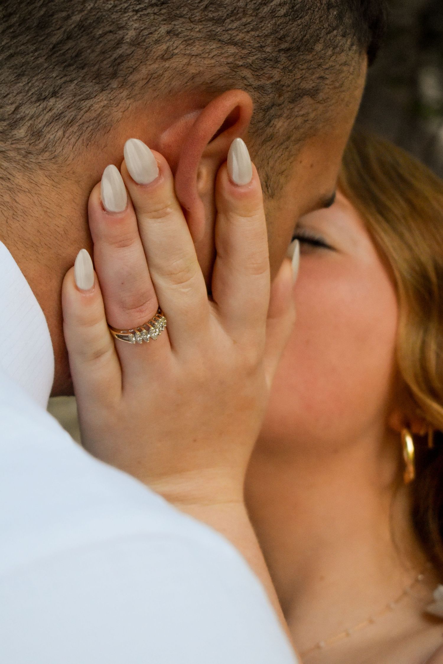 Close-up romantic shot showing white manicured nails with sparkling engagement ring during an intimate moment.