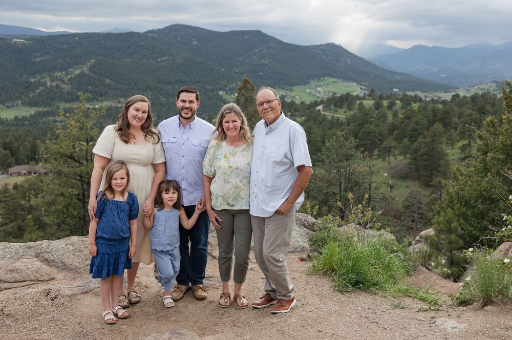Multi-generational family posing together on a mountain overlook with forest and peaks in the background.