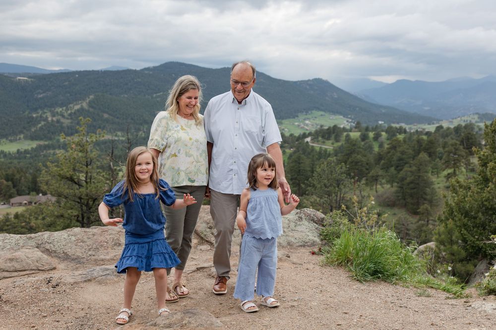 A small group stands together on a mountain viewpoint under cloudy skies with rolling hills behind them.