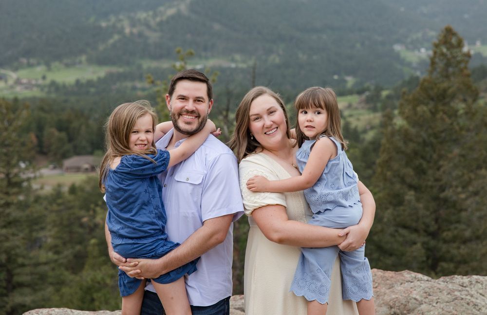 Family of four poses together on mountain overlook with scenic valley views behind them.