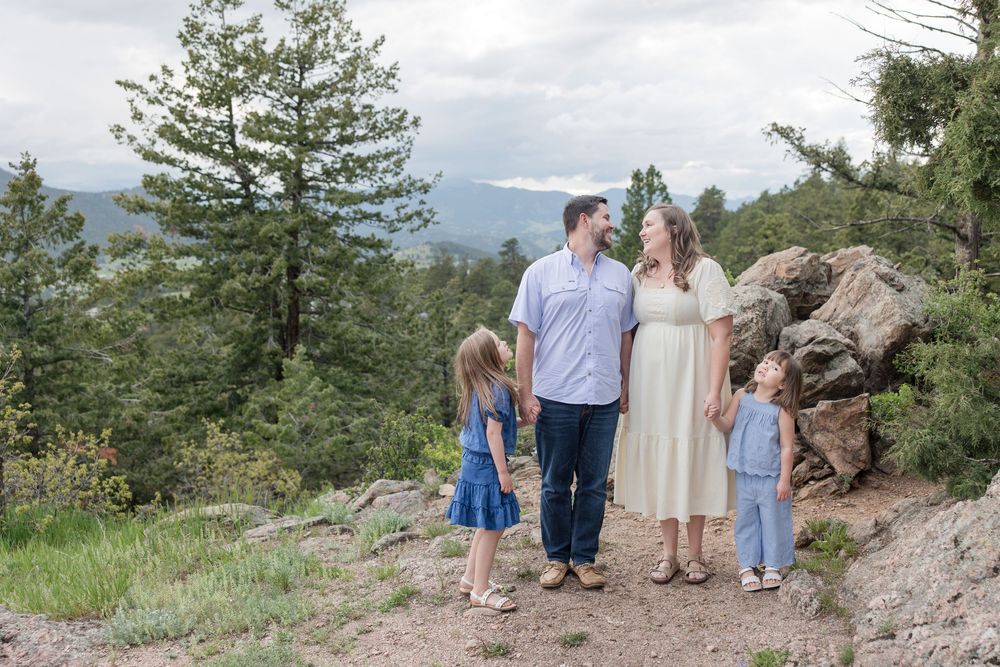 A picture of a family standing together on a rocky mountain overlook with pine trees and mountains in the background.