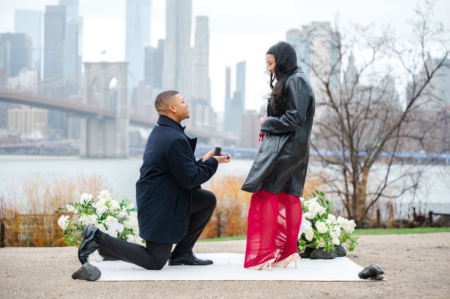 A romantic surprise proposal with the city skyline in the background as someone kneels down on one knee.