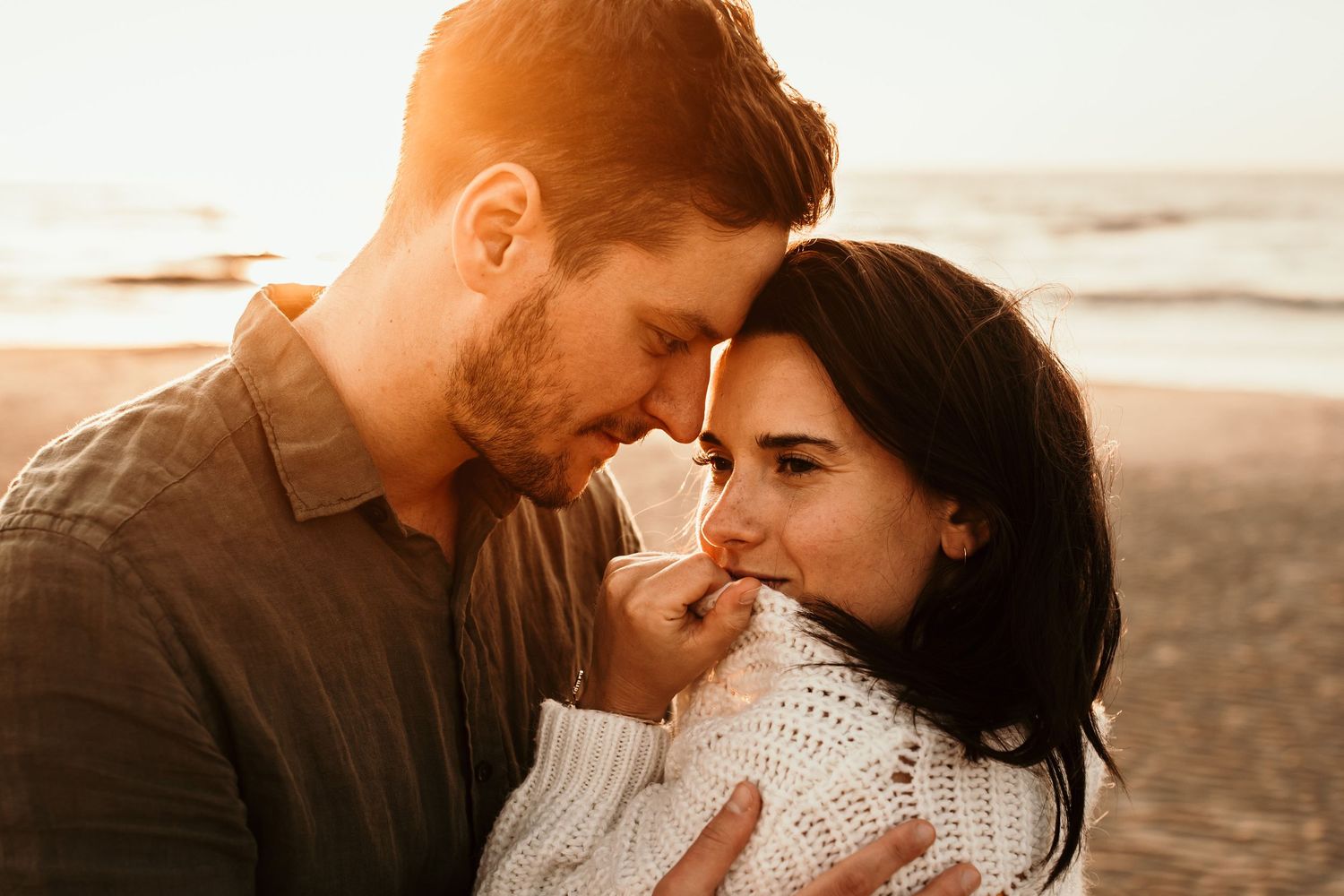 Intimate beach engagement photo during golden hour with warm tones.