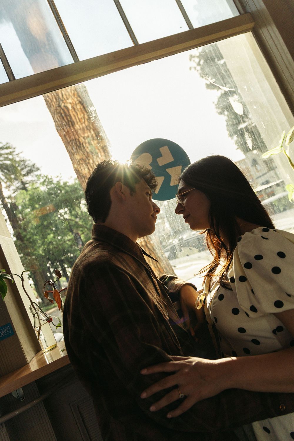 A romantic moment captured against window light with polka dot dress and brown jacket.