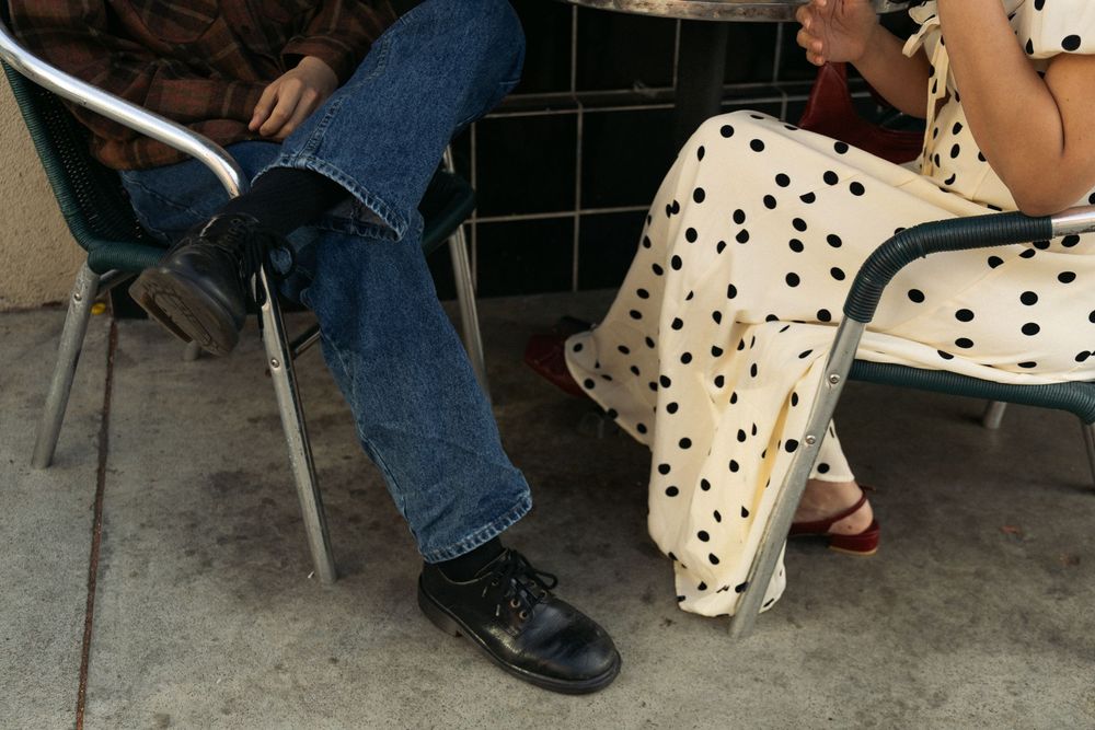 Two people sit in chairs, one wearing jeans and another in a polka dot dress.