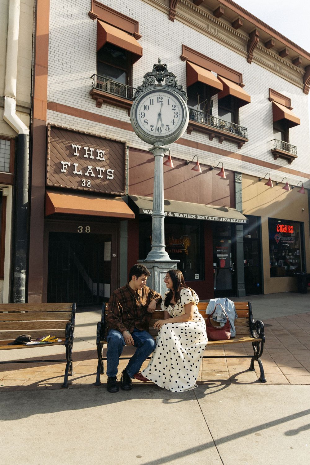 A couple sits on a bench outside The Flats building beneath a vintage clock.