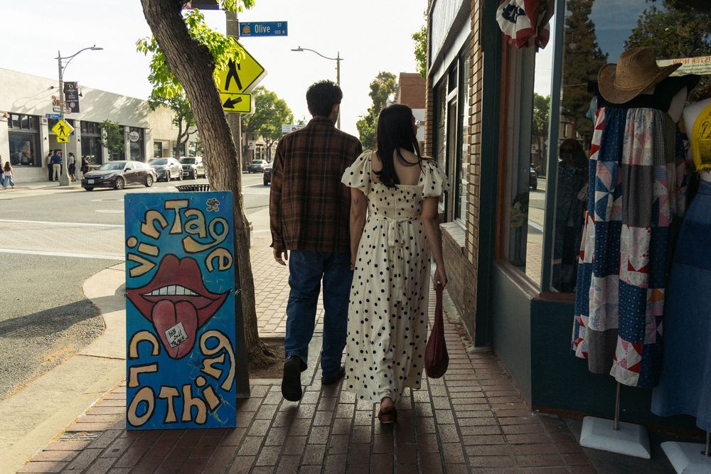 A couple window shopping while walking down a sidewalk with colorful storefront art.
