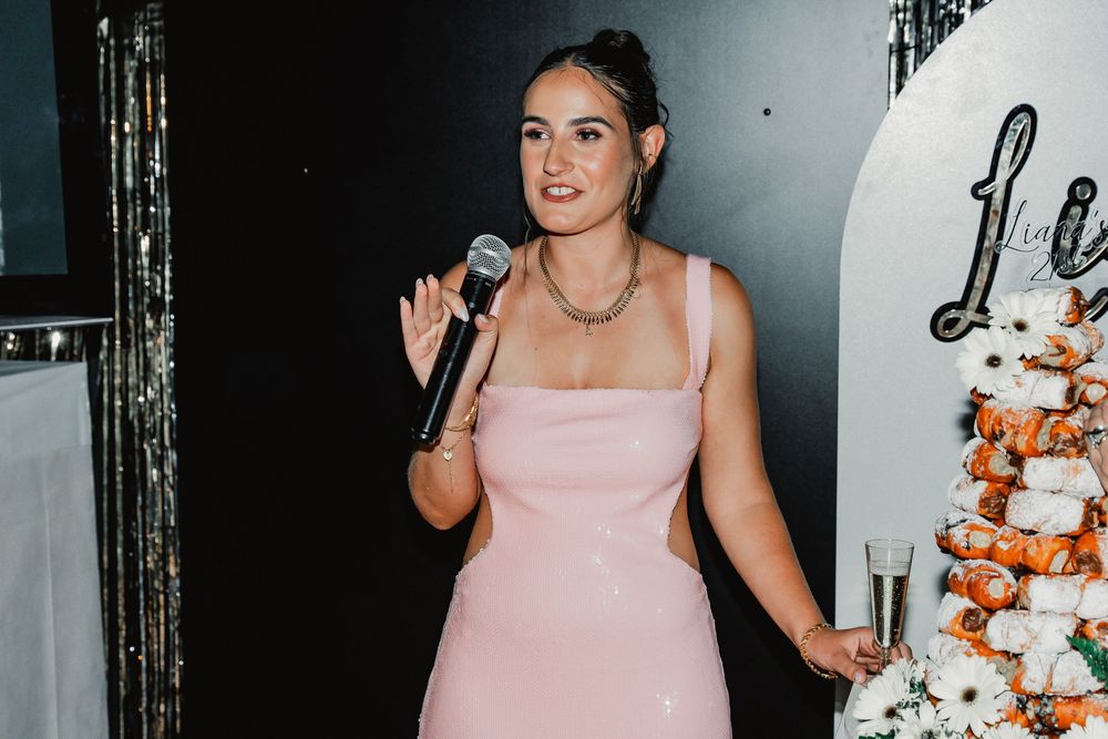 Person in a pink formal dress standing next to an elegantly decorated cake at an event.