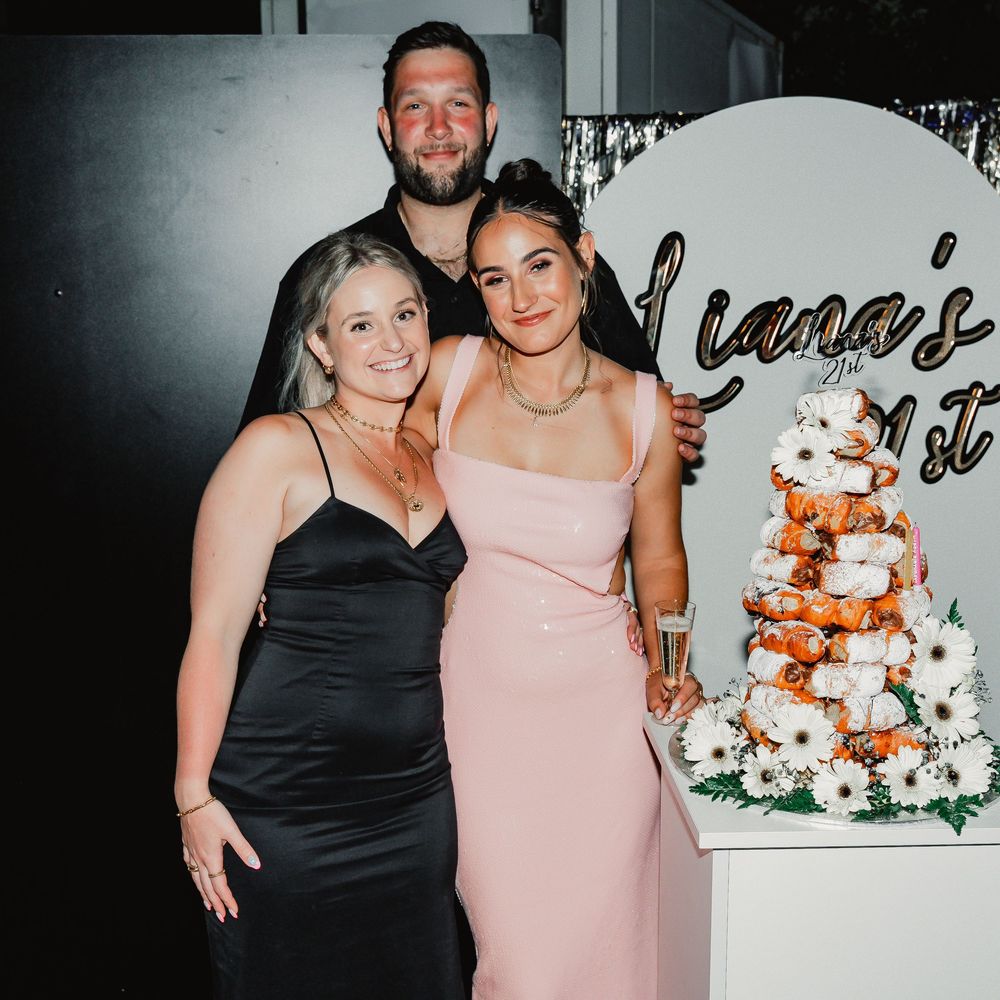 Two people in formal attire posing together at an event with black and white decor and floral arrangements.