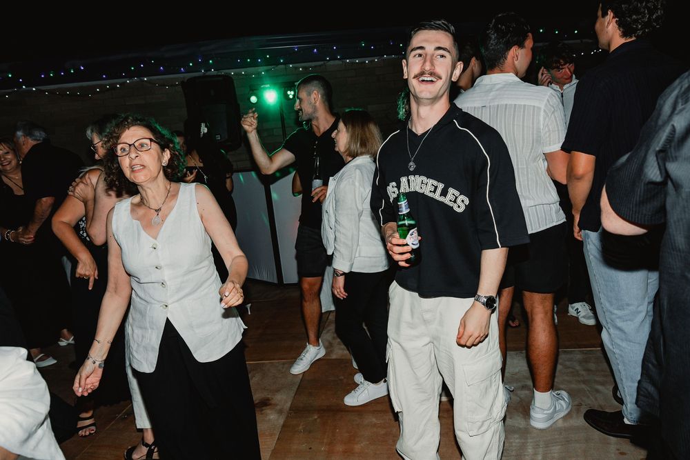 Party attendees dancing and enjoying themselves on a dance floor under colorful lighting at a nighttime event.